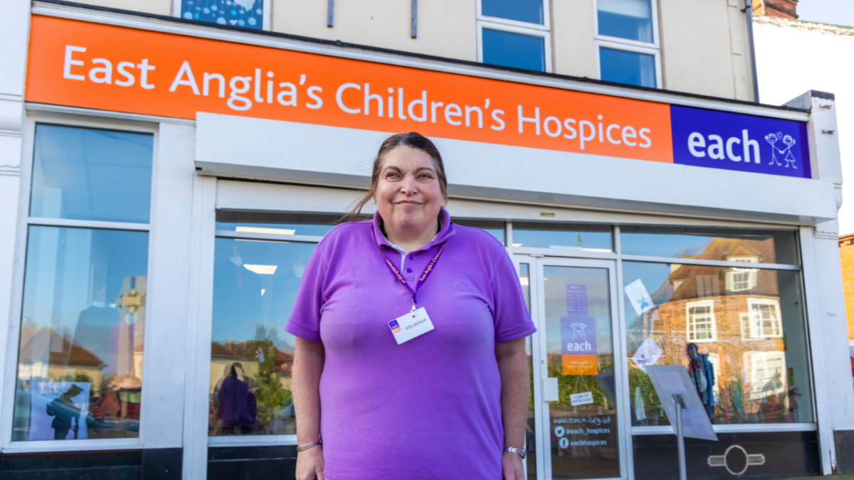 Elaine standing in front of the EACH charity shop with a volunteer badge