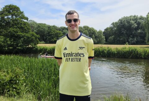 Mark smiling, standing in front of a river with a canoe passing.