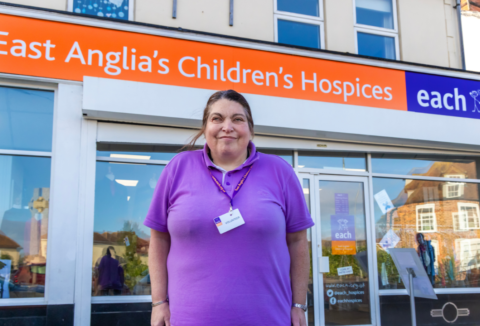 Elaine standing in front of the EACH charity shop with a volunteer badge