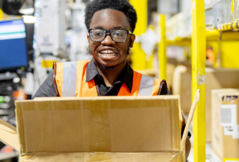 A young male intern at Amazon packing boxes and smiling.