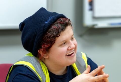 Employee at Fedex smiling, hands together, looking across the room