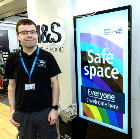Young man with autism standing next to a sign that says 'Safe Space - everyone welcome here'