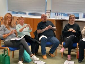A group of people sitting down and learning BSL Level 1 course - following the British Sign Language signs after the tutor.