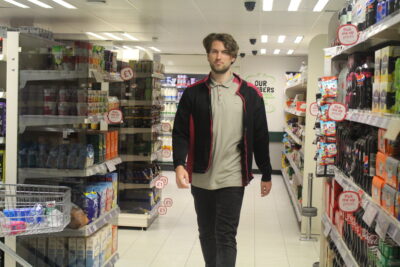 Zach in Co-op uniform walking past different shelves with products.