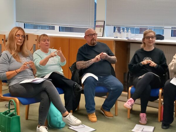A group of people sitting down and learning BSL Level 1 course - following the British Sign Language signs after the tutor.