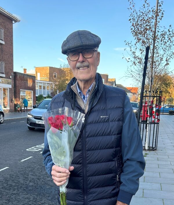 Older gentleman standing in street holding a bunch of roses smiling.