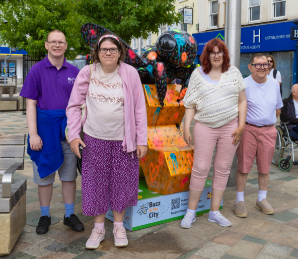 Group of people standing next to a bee sculpture