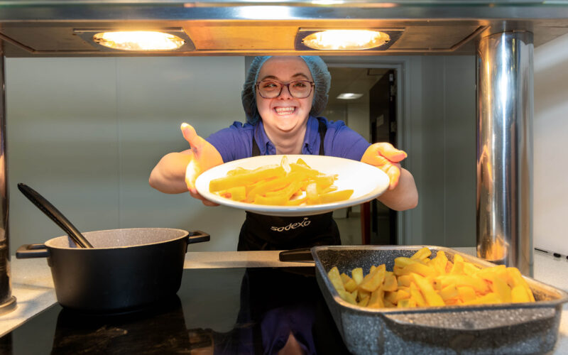 Food service assistant serving chips in a canteen