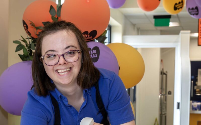 Young lady with glasses in Sodexo food service uniform clearing tables in a canteen.