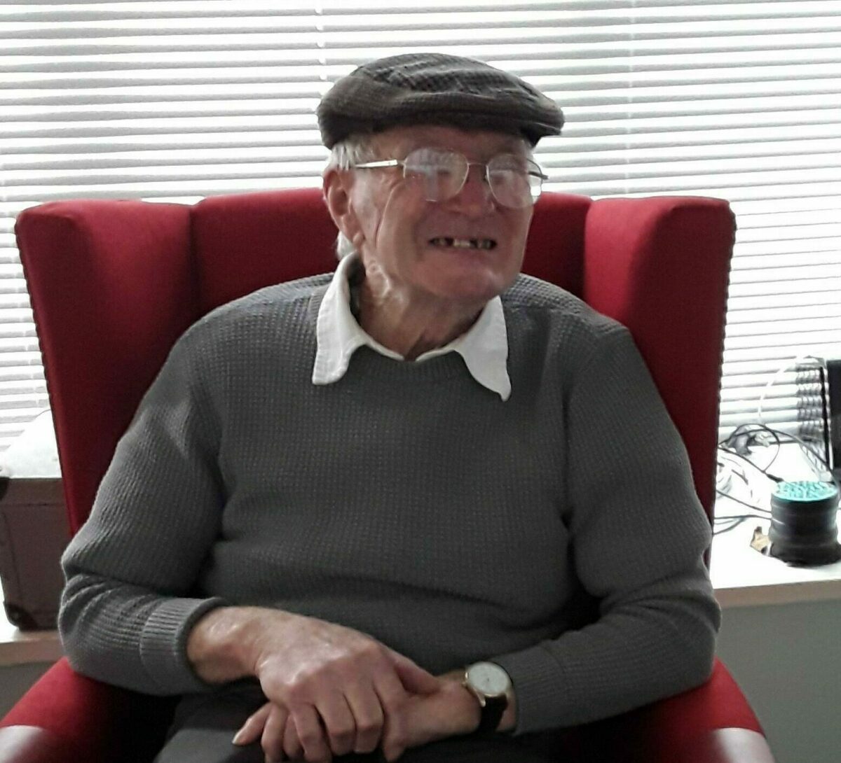 Elderly gentleman sitting down in a red armchair smiling at the camera.
