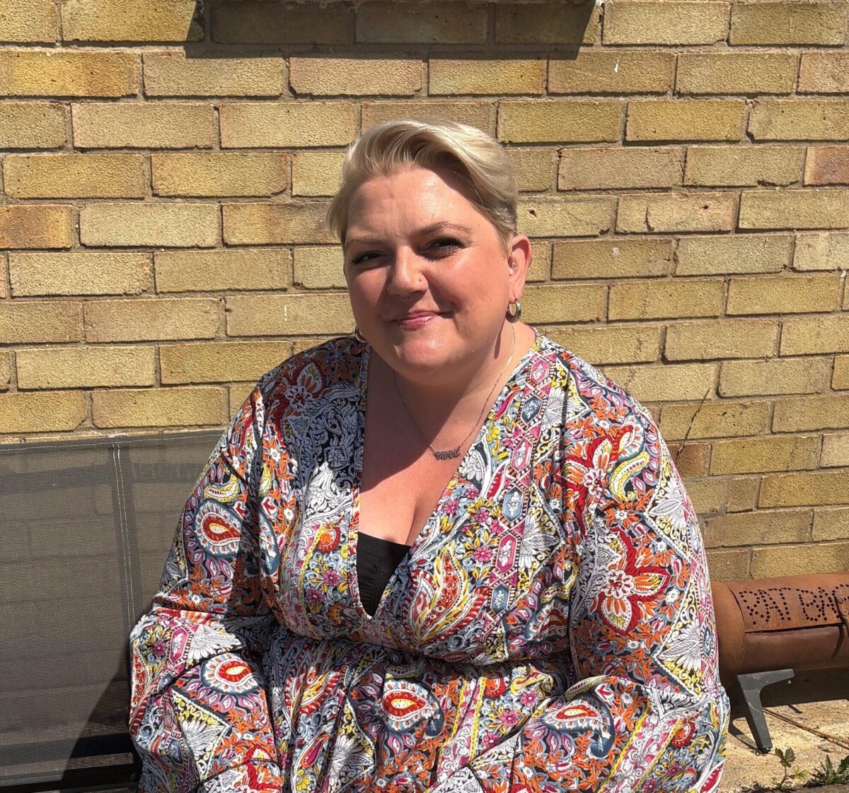Lady sitting on a bench outside a house.