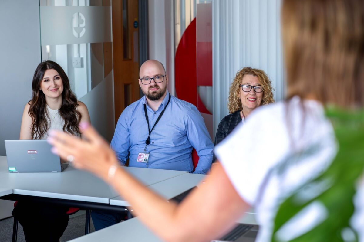 Three people sitting watching a person presenting to them