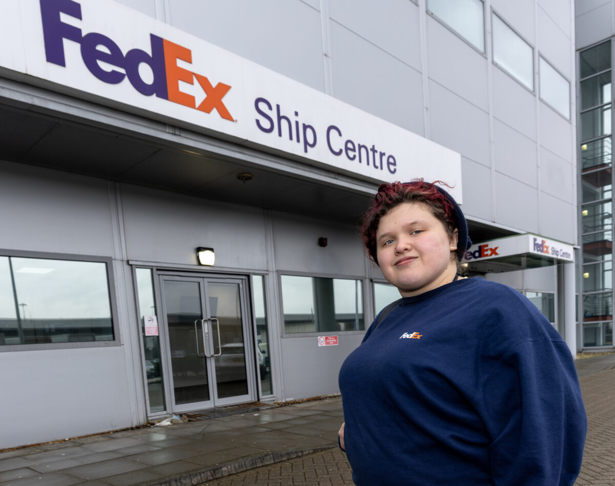 A person standing if front of a big sign on a building saying 'FedEx' Ship Centre