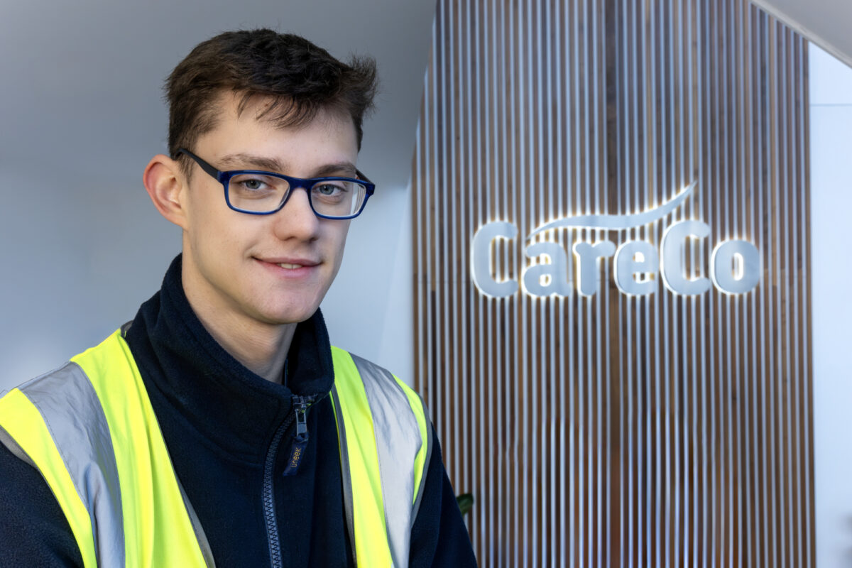 A young man in front of 'CareCo' sign wearing a high-ves