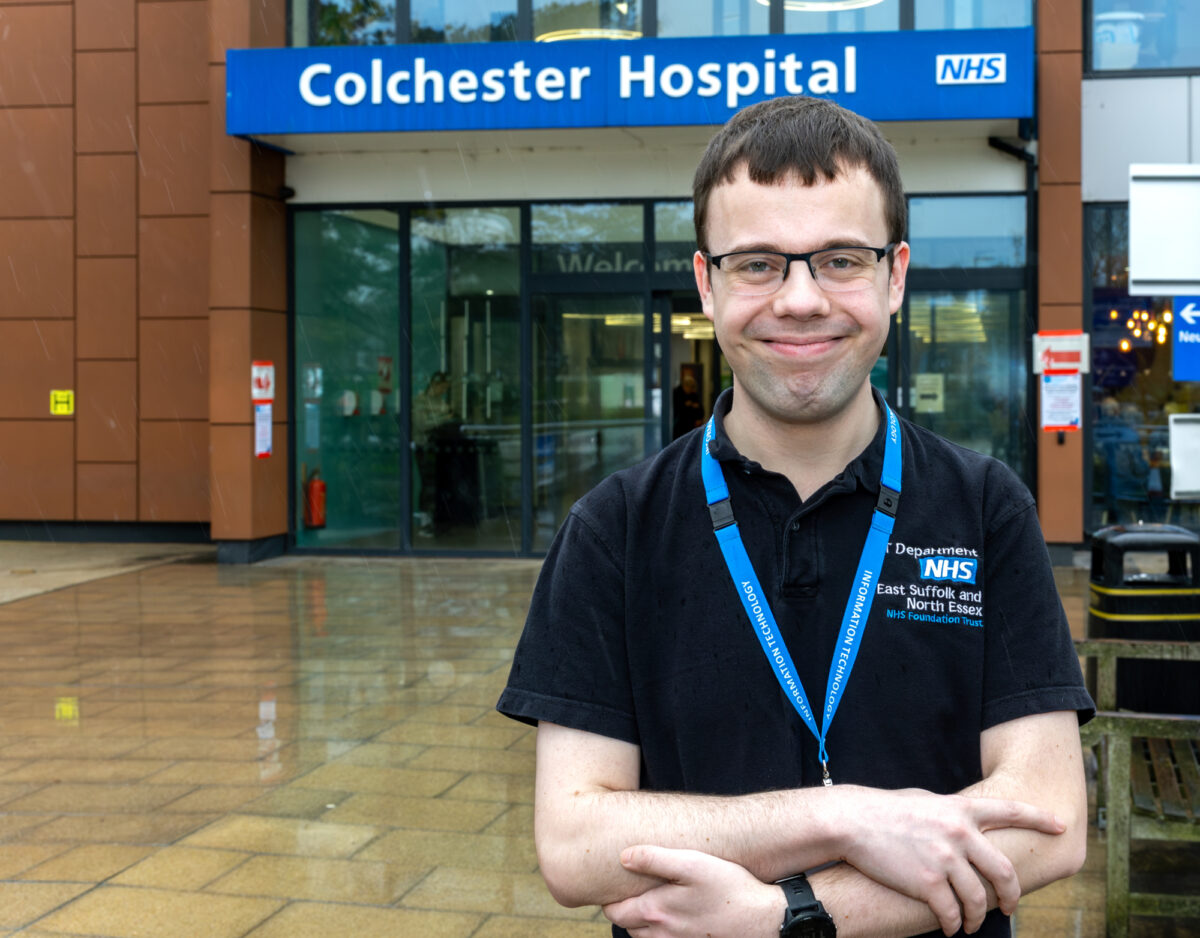 A young man standing in front of the Colchester Hospital looking at the camera and smiling
