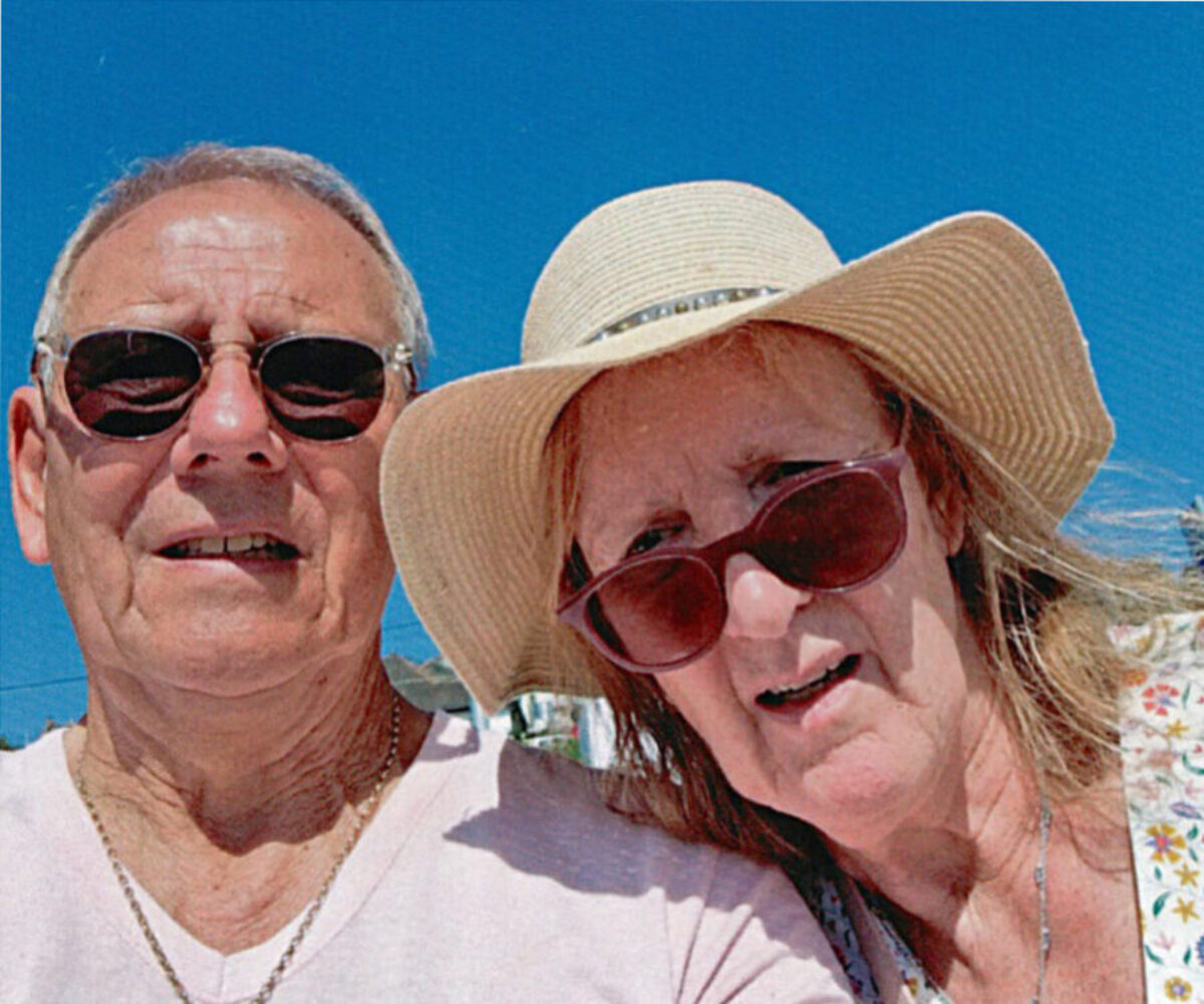 An older couple on holiday, man in sunglasses, lady in sunglasses and a hat.