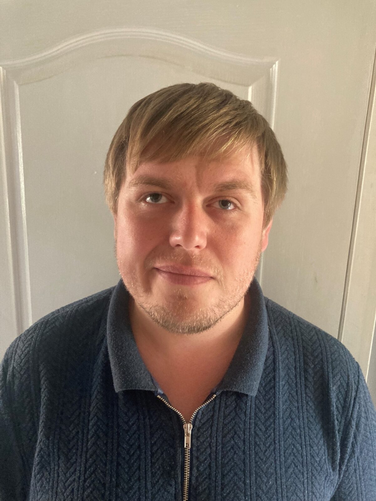 A blonde man facing the camera wearing blue polo shirt