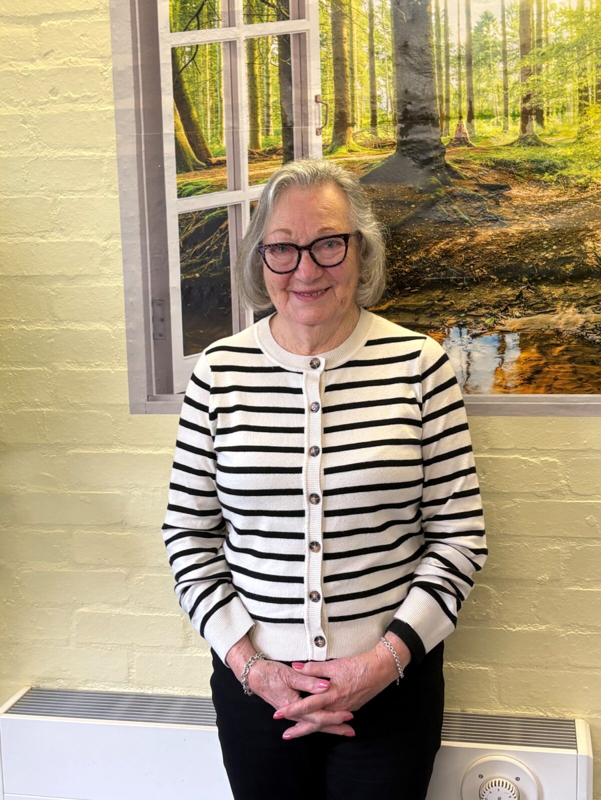 Older lady with glasses standing in front of a painting.