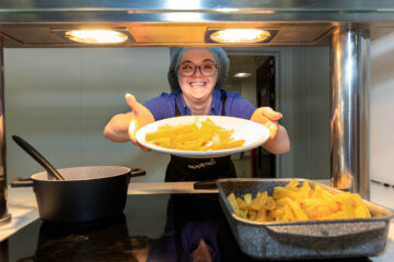 Food service assistant serving chips in a canteen