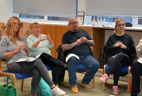 A group of people sitting down and learning BSL Level 1 course - following the British Sign Language signs after the tutor.