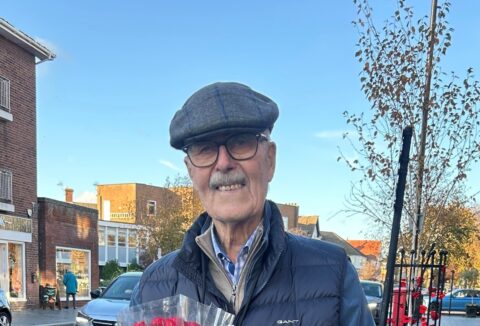 Older gentleman standing in street holding a bunch of roses smiling.