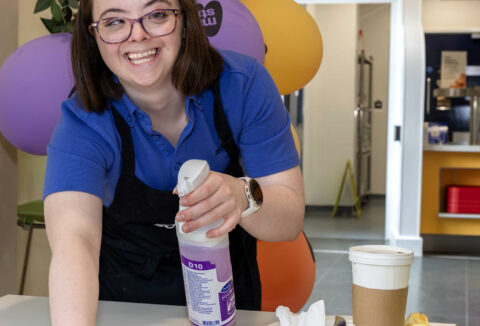 Young lady with glasses in Sodexo food service uniform clearing tables in a canteen.