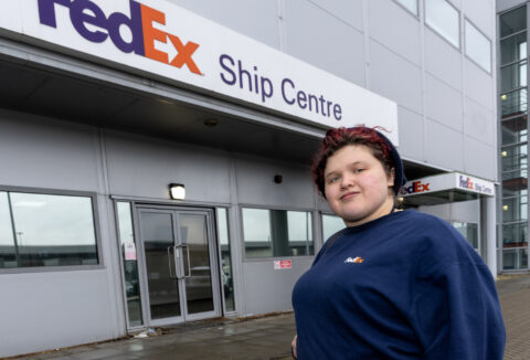 A person standing if front of a big sign on a building saying 'FedEx' Ship Centre