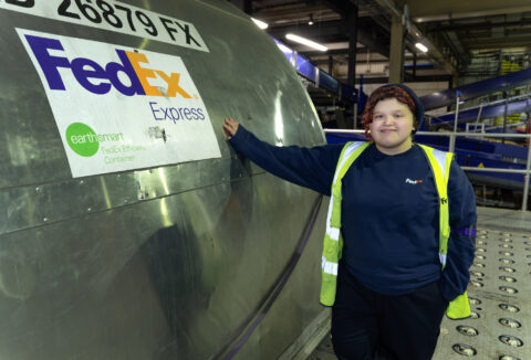 A young person in high-vis jacket standing next to a metal tank with FedEx logo on it