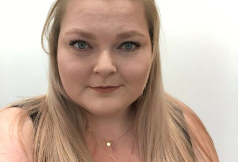 A blonde woman wearing a black tank top looking at the camera