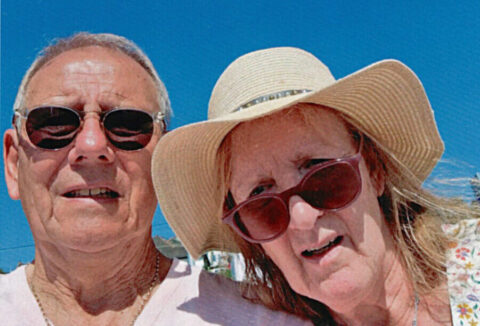 An older couple on holiday, man in sunglasses, lady in sunglasses and a hat.