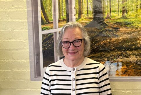 Older lady with glasses standing in front of a painting.